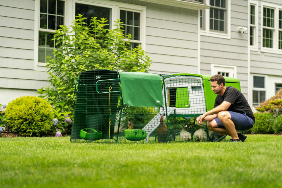 man-kneeling-next-to-eglu-cube-chicken-coop-with-run-in-front-of-a-house