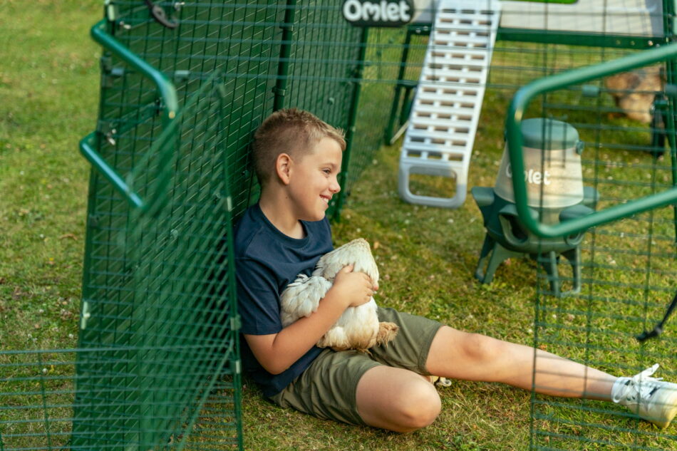 young buy cuddling a chicken in an eglu pro chicken run